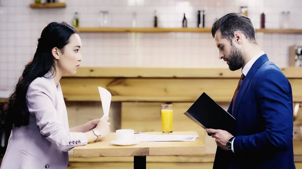 Side view of asian businesswoman looking at bearded businessman in cafe — Stock Photo