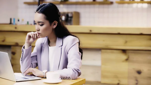 Concentré et jolie asiatique femme d'affaires en costume en utilisant ordinateur portable tout en travaillant à distance dans le café — Photo de stock