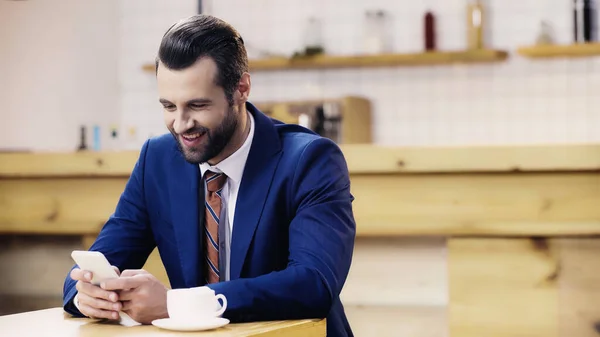 Allegro uomo d'affari in giacca e cravatta messaggistica su smartphone in caffè — Foto stock