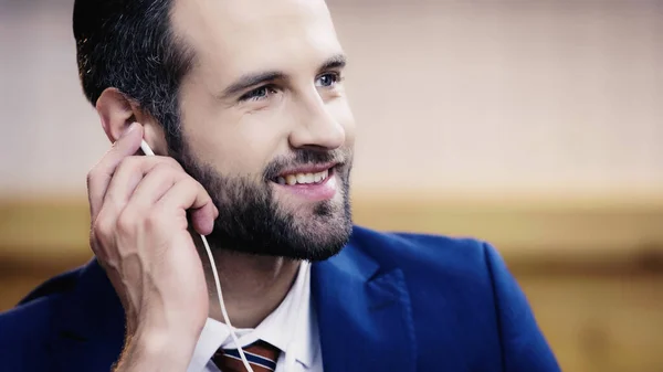 Homem de negócios barbudo sorrindo ao ajustar fone de ouvido — Fotografia de Stock