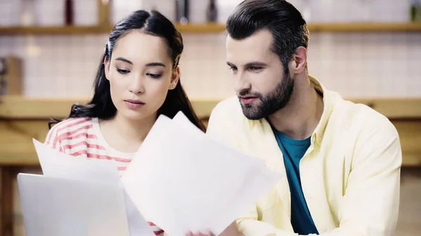 Interracial students looking at conspectus on papers in cafe — Stock Photo