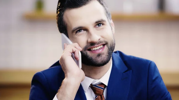 Hombre de negocios alegre en traje hablando en el teléfono inteligente en la cafetería - foto de stock