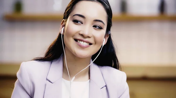 Heureux asiatique femme en costume écoute musique dans earphones — Photo de stock
