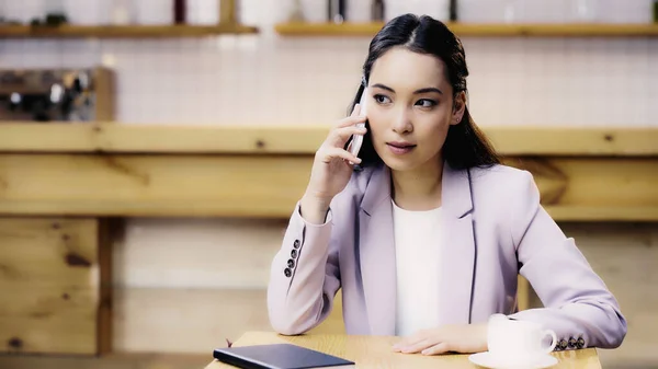 Young asian woman in suit talking on smartphone in cafe — Stock Photo