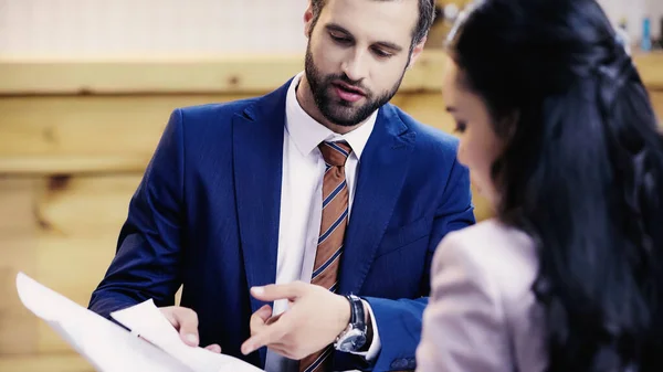 Businessman showing documents to blurred asian businesswoman in cafe — Stock Photo