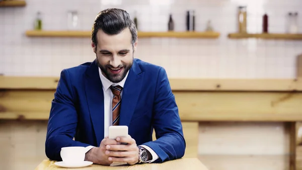 Cheerful businessman in suit using mobile phone in cafe — Stock Photo