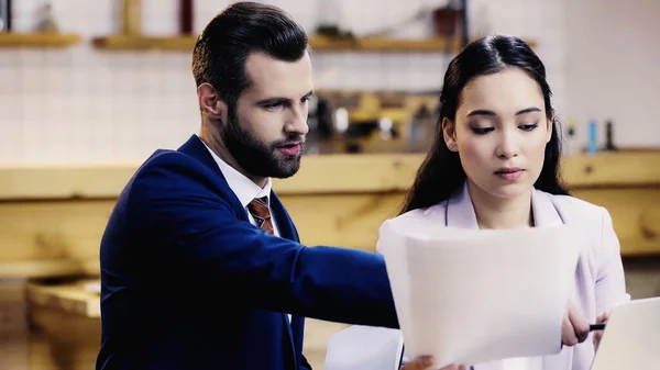 Bearded businessman talking near asian businesswoman with documents in cafe — Stock Photo