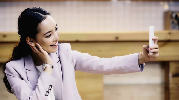Lächelnde asiatische Geschäftsfrau im Anzug macht Selfie mit dem Smartphone im Café — Stockfoto