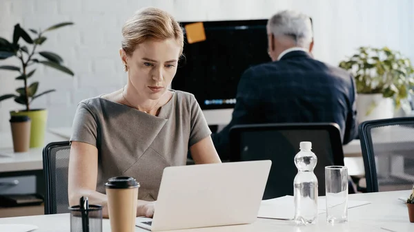 Бізнес-леді, використовуючи ноутбук біля кави і води в офісі — стокове фото