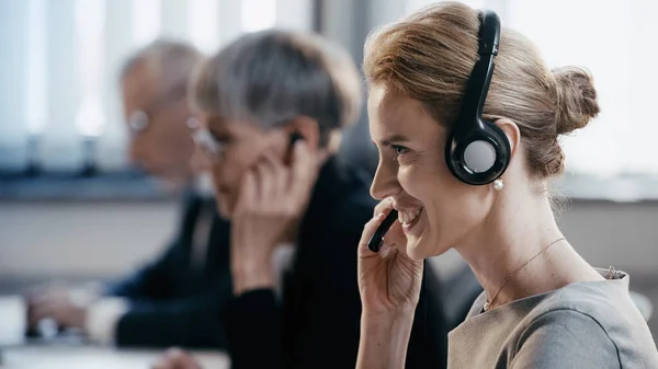 Vista lateral de empresária sorridente usando fone de ouvido no escritório — Fotografia de Stock