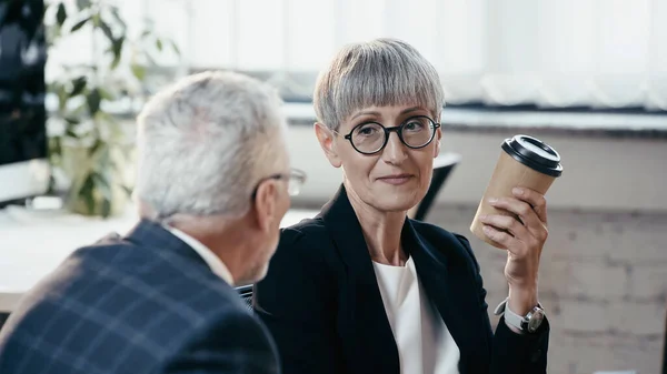 Reife Geschäftsfrau hält Pappbecher neben Kollegin im Büro — Stockfoto