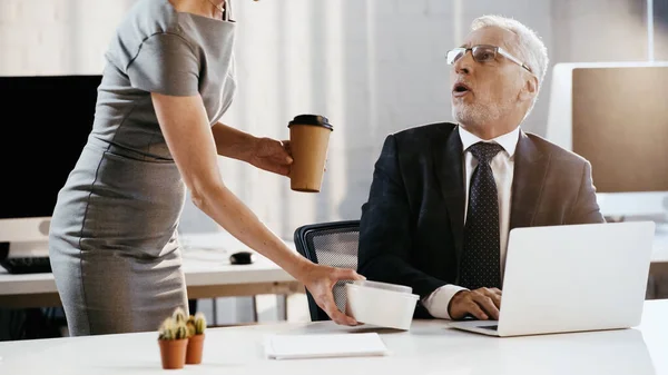 Businesswoman holding coffee to go and takeaway container near shocked colleague in office — Stock Photo