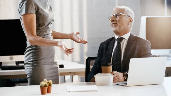 Smiling businessman looking at colleague near food and laptop in office — Stock Photo