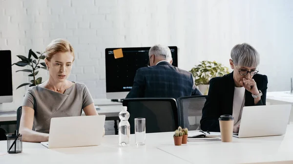 Businesswomen using laptops near drinks in office — Stock Photo