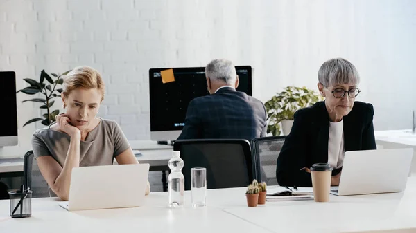 Businesswomen in formal wear using laptops near colleague in office — Stock Photo