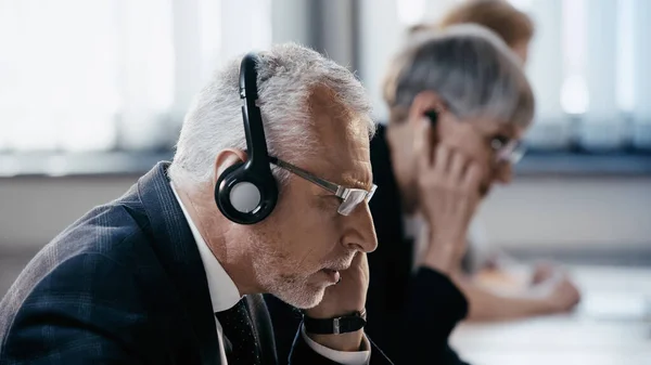 Vista lateral de hombre de negocios de mediana edad en auriculares trabajando en la oficina - foto de stock
