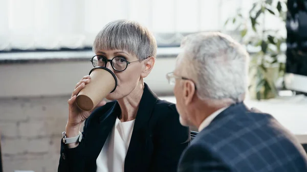 Donna d'affari di mezza età che beve caffè per andare a guardare il collega in carica — Foto stock