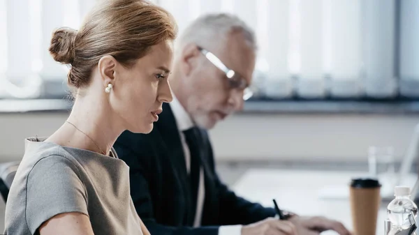 Side view of businesswoman sitting near laptop and water in office — Stock Photo