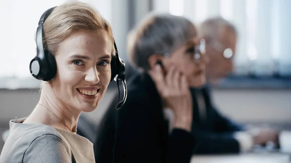 Femme d'affaires souriante dans un casque regardant la caméra dans le bureau — Photo de stock