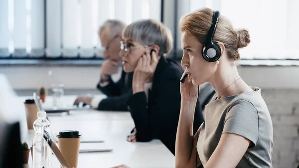 Vista lateral da mulher de negócios no fone de ouvido falando perto do laptop no escritório — Fotografia de Stock