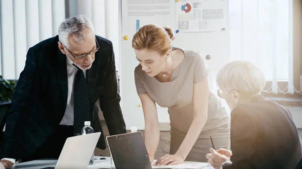 Gente de negocios en ropa formal trabajando con papeles cerca de computadoras portátiles en la oficina - foto de stock