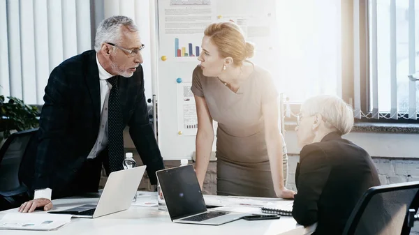 Business people talking during meeting near laptops and papers in office — Stock Photo