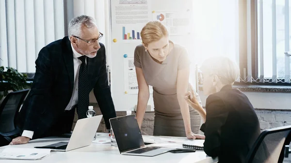 Mature businesswoman pointing with finger near colleagues during meeting in office — Stock Photo