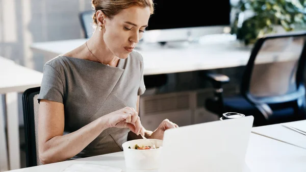 Businesswoman sitting near takeaway salad, laptop and coffee to go in office — Stock Photo