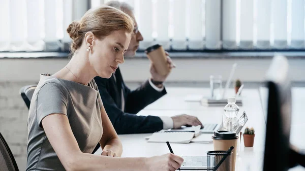 Side view of businesswoman holding pen near laptop and coffee to go in office — Stock Photo