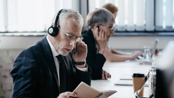 Homme d'affaires mature dans un casque regardant un ordinateur portable près du bureau — Photo de stock