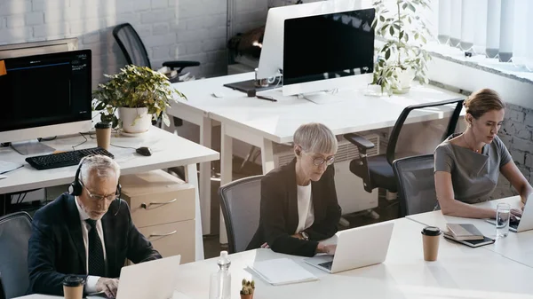 Vue grand angle des hommes d'affaires utilisant des ordinateurs portables près des ordinateurs portables dans le bureau — Photo de stock