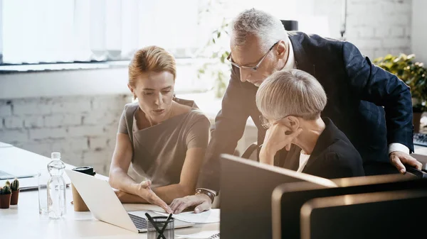 Empresaria señalando papel cerca de colegas y portátil en la oficina - foto de stock