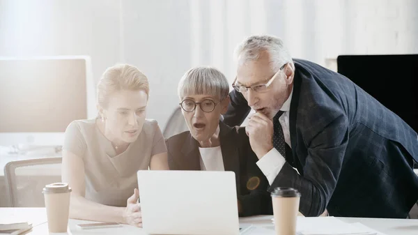 Shocked business people looking at laptop near papers in office — Stock Photo