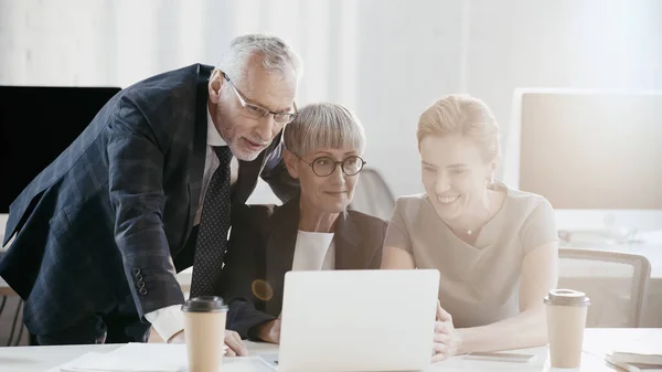 Gente de negocios positiva sentada cerca de dispositivos y café en la oficina - foto de stock