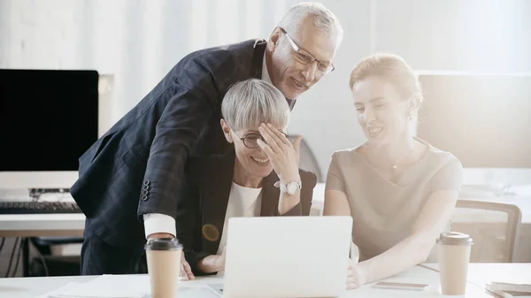 Gli uomini d'affari positivi che guardano il computer portatile vicino al caffè offuscato per andare in ufficio — Foto stock