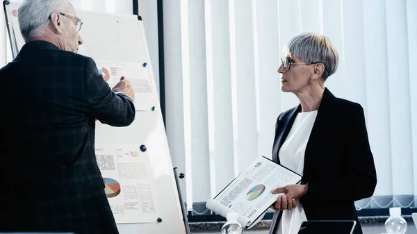 Les gens d'affaires matures travaillant avec des documents sur tableau à feuilles mobiles dans le bureau — Photo de stock