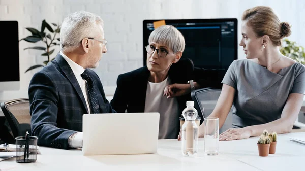 Empresários em uso formal conversando perto de laptop e papéis no escritório — Fotografia de Stock