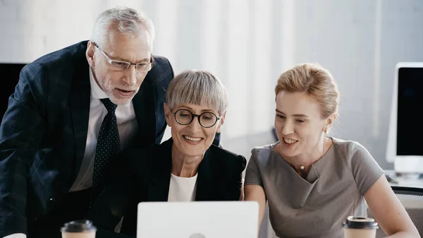 Positive business people in formal wear looking at blurred laptop in office — Stock Photo