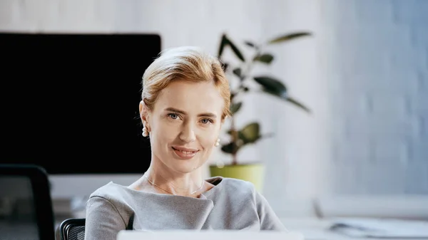 Lächelnde Geschäftsfrau blickt im Büro in die Kamera — Stockfoto