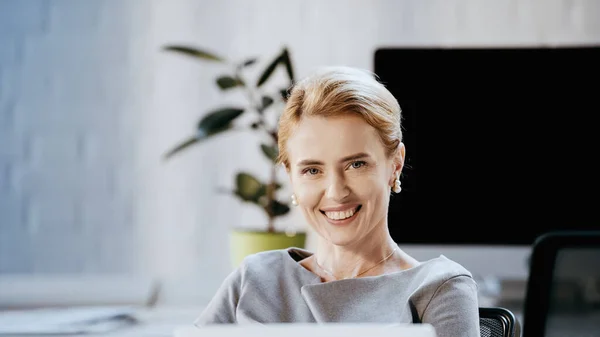 Cheerful businesswoman in formal wear looking at camera in office — Stock Photo