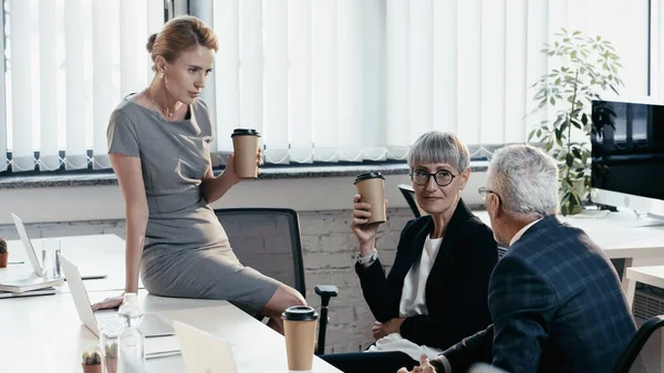 Managers in formal wear holding takeaway cups near laptops in office — Stock Photo