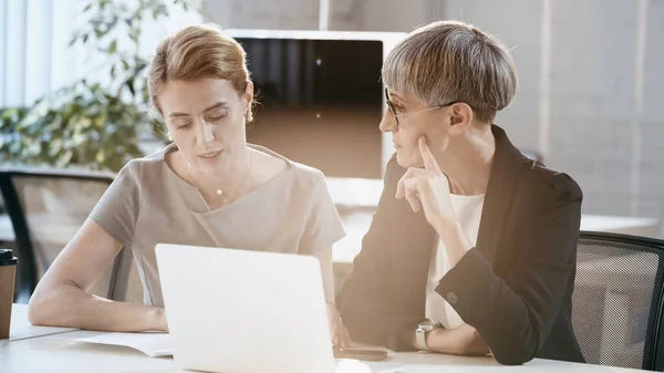 Donna d'affari che parla con un collega vicino a documenti e dispositivi in ufficio — Foto stock