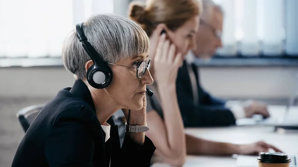 Mulher de negócios madura em óculos e fone de ouvido trabalhando no escritório — Fotografia de Stock