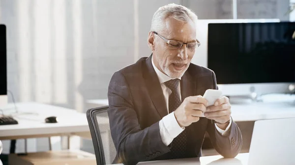 Uomo d'affari sorridente che utilizza il cellulare mentre lavora in ufficio — Foto stock