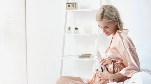 Довольная беременная женщина с беспроводными наушниками рядом с животом — стоковое фото