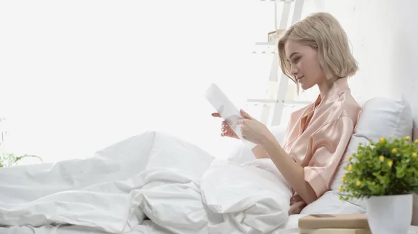 Side view of pleased blonde woman using digital tablet in bedroom — Stock Photo