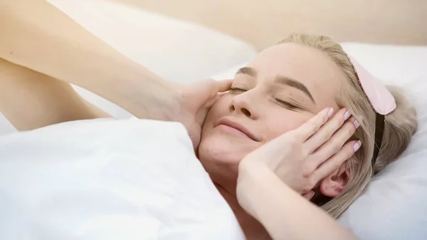 Cheerful blonde woman with sleeping mask waking up in bed — Stock Photo