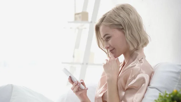 Vista laterale della donna allegra che chatta sullo smartphone in camera da letto — Foto stock