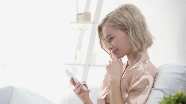 Side view of cheerful woman chatting on smartphone in bedroom — Stock Photo