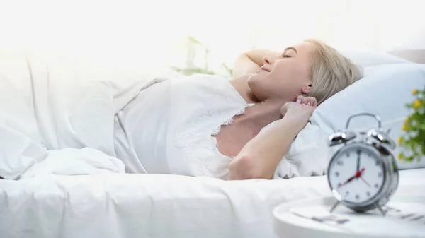 Young blonde woman lying in bed, stretching and smiling in bedroom — Stock Photo